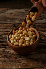Old and rusty wooden table with a wooden bowl with shelled peanuts and some peanuts and in the wooden ladle, selective focus