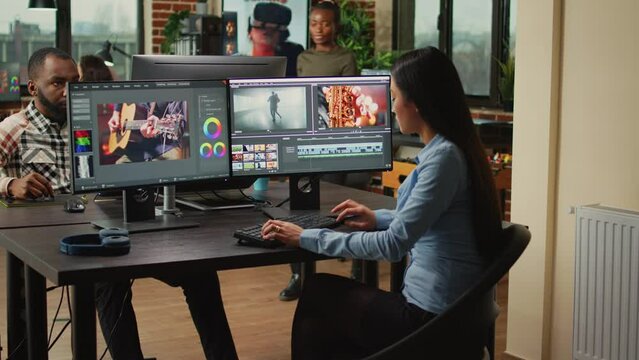 Asian film maker working on movie footage quality with editing software, using multiple monitors in agency studio. Post production house creative artist creating audio and video montage.