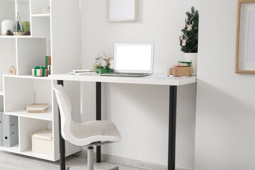 Workplace with laptop, Christmas tree and presents in light office