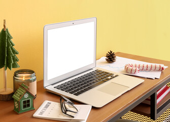 Laptop with Christmas toys and candle on table near yellow wall