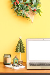 Laptop with Christmas toys and candle on table near yellow wall