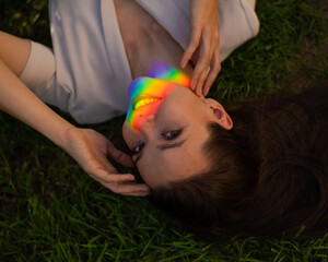 Top view of caucasian woman with rainbow ray on her face lies on green grass. 