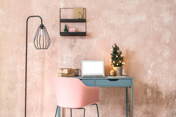 Workplace with laptop, Christmas tree and gifts near pink wall