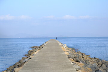 People fishing at the end of a breakwater on a clear blue sky day in the Seto Inland Sea.