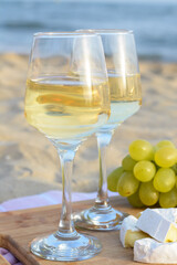 Glasses with white wine and snacks for beach picnic on sandy seashore
