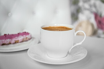 Cup of delicious aromatic coffee and eclair on white table indoors, closeup