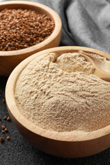 Fototapeta na wymiar Buckwheat flour and grains in bowls on black table, closeup