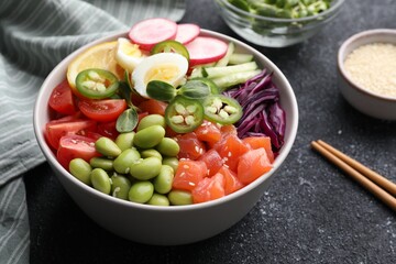 Poke bowl with salmon, edamame beans and vegetables on black table