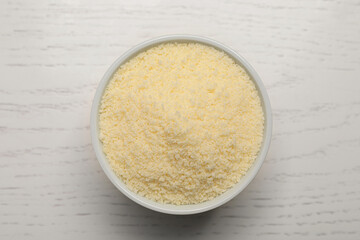Delicious grated parmesan cheese in bowl on white wooden table, top view