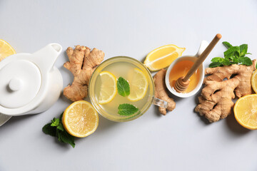 Delicious ginger tea and ingredients on light grey background, flat lay