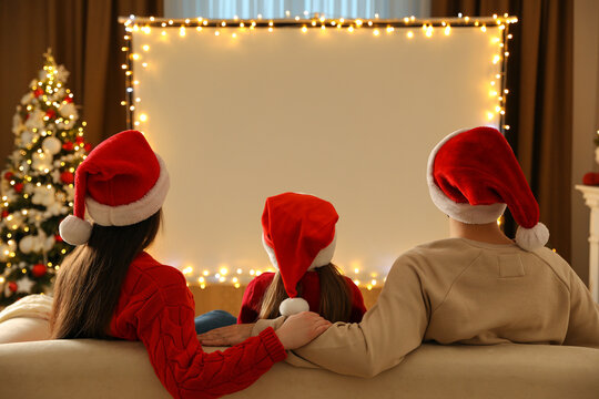 Family watching movie on projection screen in room decorated for Christmas, back view. Home TV equipment