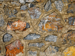 Old stone wall close up in orange beige blue grey palette. Stone tile with cement joints background with detailed natural texture. Historical building facade.