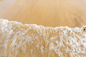Ocean beach aerial top down view with water, waves with foam and spray and fine sand, beautiful summer vacation holidays