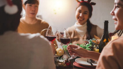 Group of young Asian friends cheers wine glasses to celebrate Christmas Eve dinner. Party of asian Friends Enjoying Drinks and celebrating. close up glasses of clinking glasses of wine with happiness.