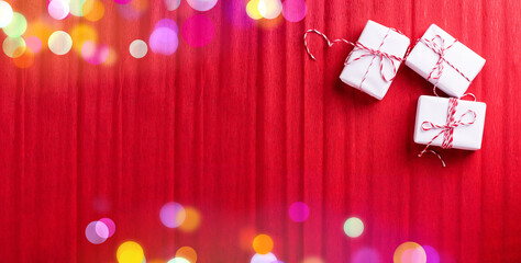 Banner with three wrapped boxes with presents  and bokeh lights on  red textured  paper background.  Place for text. Top view. - 550744950