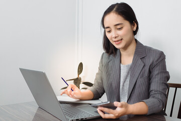 Happy businesswoman sitting at desk behind her laptop and look  with somebody on her mobile phone while working at office.