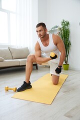 Fototapeta na wymiar Man sports home training on the floor on a mat with dumbbells, exercises for muscle growth, pumped up man fitness trainer exercises at home, the concept of health and beauty of the body