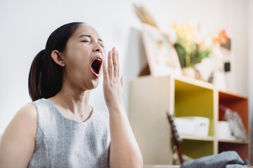 Asian woman yawning while working on laptop in her office.