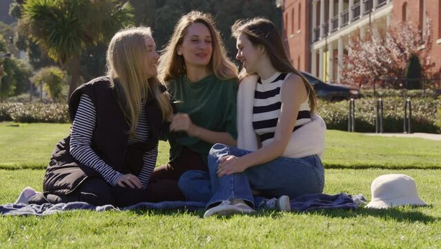 Portrait of caucasian women with long hair resting on the lawn of green city park. Cheerful girls in their 30s enjoying good, weekend time together. High quality 4k footage