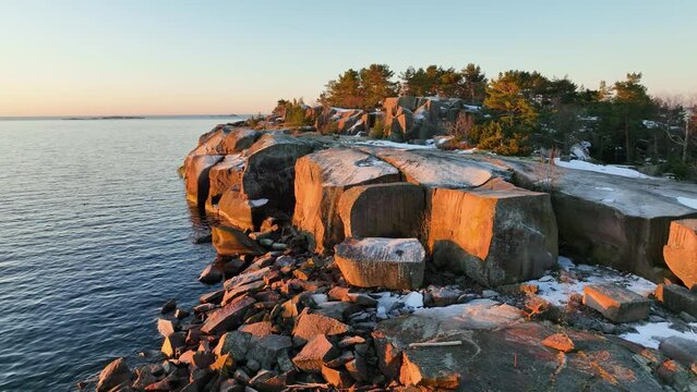 Aerial view around the snowy and rocky coast of Hanko, spring sunrise in southern Finland