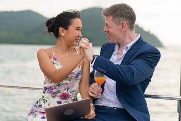 Caucasian businessman and businesswoman working outdoor together on digital tablet for online corporate. Two luxury business people working with laptop on a sailing boat. Concept business travel