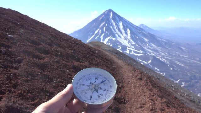 A trip to the volcanic plateaus of Kamchatka. Compass in the hand of a hiker (orientation by the aid of a compass). Volcanoes in the background.