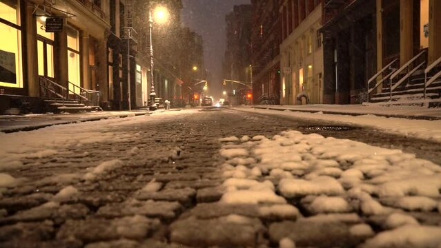 Snowy cobble stone street in Soho, Manhattan is lit by street lights shorty before sunrise