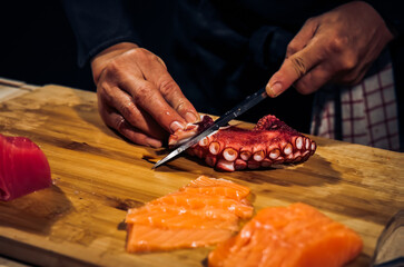 Close up of Chef cook hands chopping octopus for traditional Asian cuisine with Japanese knife. Professional Sushi chef cutting seafood japanese chefs are making octopus sashimi. Dark Tone