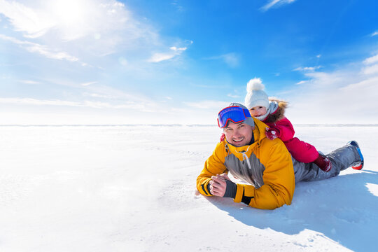Portrait of dad and daughter in the snow. Man with a small kid have fun together on a sunny frosty day. They fool around and laugh against the blue sky.