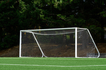 Empty soccer goal with white net on a sunny day, artificial turf field
