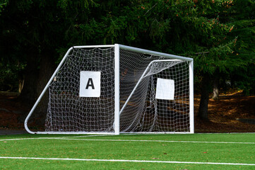 Empty soccer goal with white net on a sunny day, artificial turf field
