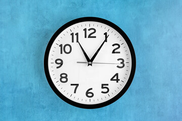 Modern analog clock, round in black and white, on a blue background
