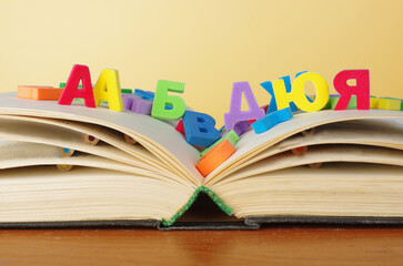 Alphabet. An open book with colored letters of the Russian alphabet scattered across it.