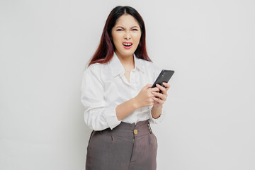 Naklejka premium A dissatisfied young Asian woman looks disgruntled wearing white shirt irritated face expressions holding her phone