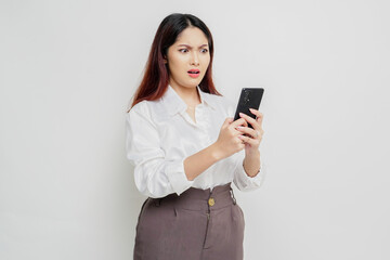 Naklejka premium A dissatisfied young Asian woman looks disgruntled wearing white shirt irritated face expressions holding her phone