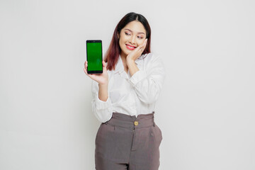 Excited Asian woman wearing white shirt pointing at the copy space beside her while holding her phone, isolated by white background