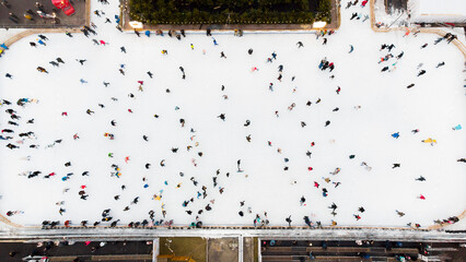 Top view of people skating on large open air ice rink on winter day. Aerial Drone View Flight Over crowd of people who skate on ice at rink. Winter sport activities. Skating background. City Ice Rink.