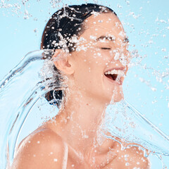 Skincare, facial and woman with water, beauty or splash in shower for cleaning, wellness or relax on blue background. Face, water splash and girl, happy and isolated in studio for hydration aesthetic