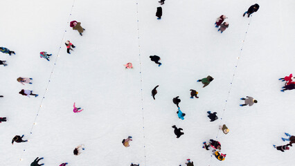 Top view of people skating on large open air ice rink on winter day. Aerial Drone View Flight Over crowd of people who skate on ice at rink. Winter sport activities. Skating background. City Ice Rink.