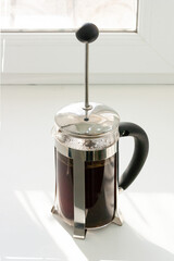 coffee is brewed in a french press, the shadow from the window