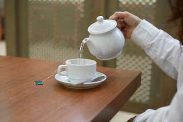 A girl pours green tea into a mug while sitting at a table indoors