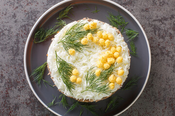 Tasty layered salad with saury, onion, potatoes, carrot, cheese, eggs and mayonnaise closeup on the plate on table. Horizontal top view from above