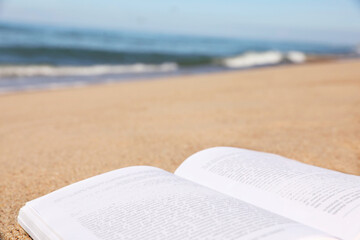 Open book on sandy beach near sea, closeup. Space for text