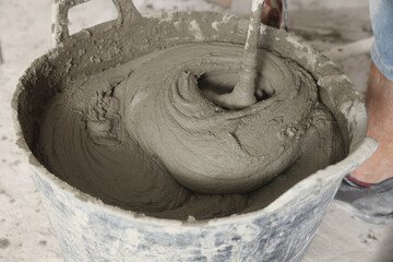 Worker mixing cement in bucket, closeup view