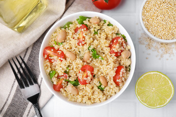 Delicious quinoa salad with tomatoes, beans and parsley served on white tiled table, flat lay