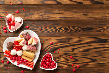 Valentine's Day concept. Top view photo of heart shaped dishes with sweets candies and cookies on wooden desk background with empty space