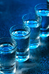 Wet glasses of vodka in smoke on dark blue background.