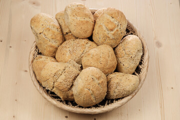 Ein Korb / Brotkorb mit frischen Sesambrötchen - Traditionell von Hand (handwerklich) gebackene knusprige Brötchen auf hellem Holz