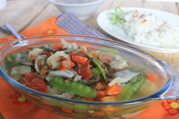 indonesian soup made of carrot, meatball,kapri, mushroom, macaroni, and tomato in oval glass bowl on wooden table

