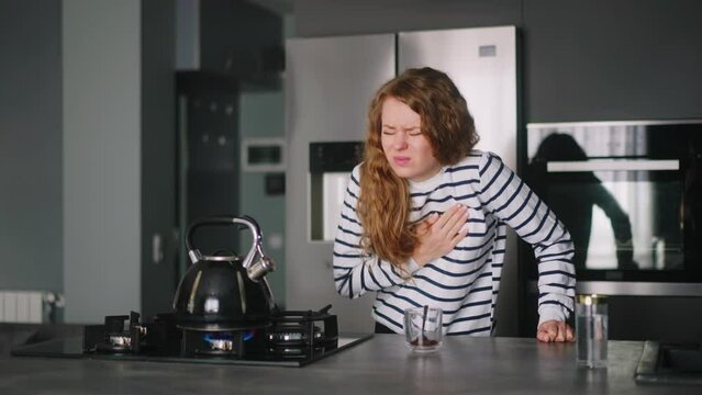 Curly woman has a heart attack doing coffee, taking pills. Adult female boiling water, feels pain in her chest, takes medicine. Girl cooking dinner and experiences pain in heart, drinks drugs.